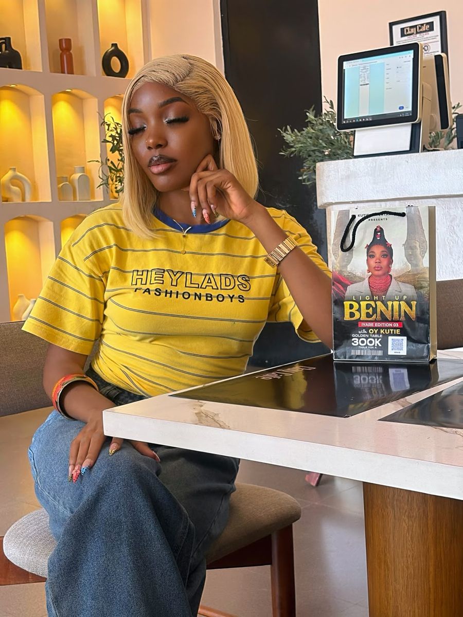 OY Kutie in a yellow striped tee, seated beside a Light Up Benin gift bag
