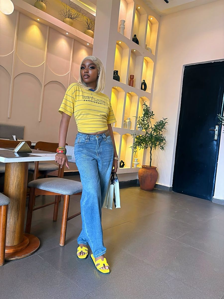 OY Kutie standing in yellow tee, jeans and yellow sandals